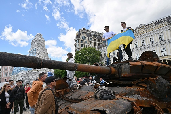 Les gens tiennent le drapeau ukrainien sur un char, lors de l'ouverture d'une exposition d'équipements militaires russes détruits dans le centre de la capitale ukrainienne de Kiev le 28 mai 2022. Photo de Sergei SUPINSKY / AFP via Getty Images.
