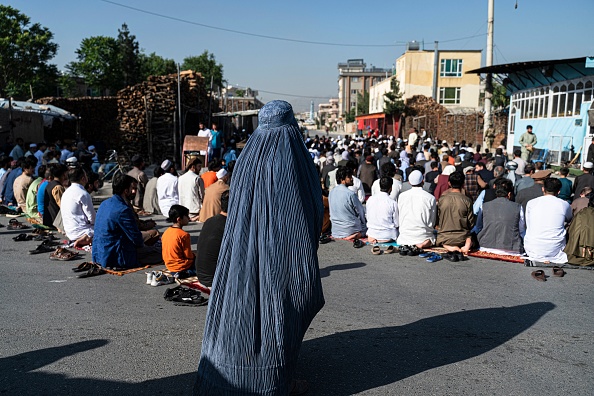 Une femme afghane vêtue d'une burqa se tient debout derrière des fidèles musulmans, devant une mosquée dans une rue de Kaboul le 1er mai 2022. Photo de WAKIL KOHSAR/AFP via Getty Images