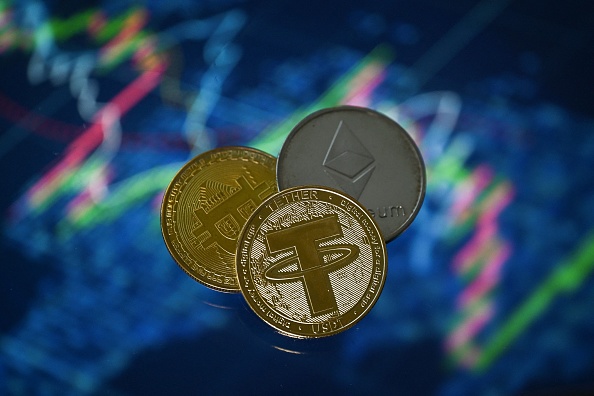 Les crypto-monnaie souvenir plaquée or Tether, des pièces de Bitcoin et d'Etherium disposées à côté d'un écran affichant un graphique de négociation. (Photo : JUSTIN TALLIS/AFP via Getty Images)