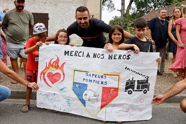 Un pompier pose avec un enfant derrière une banderole sur laquelle on peut lire "merci à nos héros" à Saint-Michel-de-Rieufret, dans le sud-ouest de la France, le 22 juillet 2022.   (ROMAIN PERROCHEAU/AFP via Getty Images)