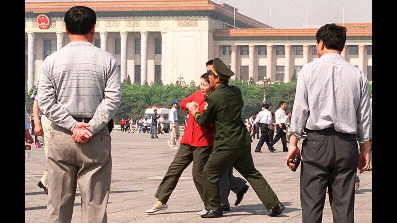Des policiers en civil regardent un officier de police chinois emmener de force une pratiquante de Falun Gong dans un fourgon de police, le 11 mai 2000, sur la place Tiananmen à Pékin. (Stephen Shaver/AFP via Getty Images) 