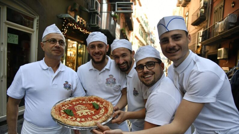 Des pizzaiolos napolitains posent avec une pizza célébrant la décision de l'UNESCO de faire de l'art du Pizzaiolo napolitain un patrimoine culturel immatériel, le 7 décembre 2017, devant la Pizzeria Brandi à Naples. (TIZIANA FABI/AFP via Getty Images)
