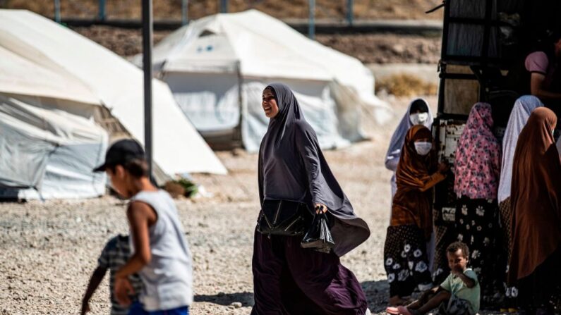 Une femme passe devant d'autres personnes rassemblées à l'arrière d'un pick-up au Camp Roj, qui abrite les membres des familles des personnes accusées d'appartenir au groupe État islamique (EI) qui ont été déplacées du camp d'al-Hol, dans la campagne près d'al-Malikiyah (Derik), dans la province de Hasakah (nord-est de la Syrie), le 30 septembre 2020. (Photo by DELIL SOULEIMAN/AFP via Getty Images)
