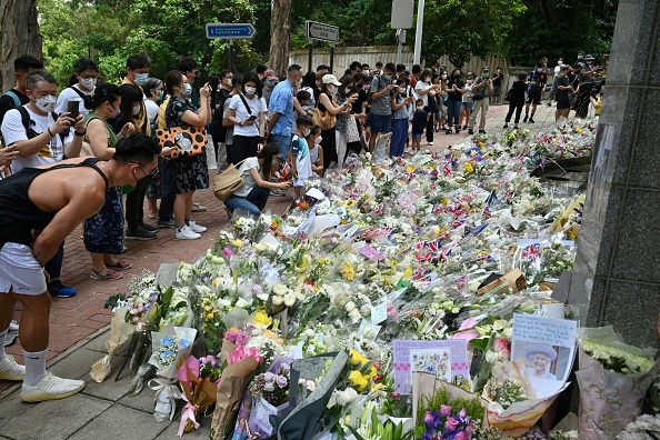 Les gens se rassemblent à côté des fleurs placées en hommage à la reine Elizabeth II devant le consulat britannique à Hong Kong le 12 septembre 2022. Photo de Peter PARKS / AFP via Getty Images.