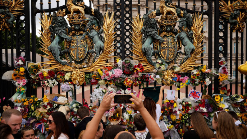 Des personnes prennent des photos et déposent des fleurs aux portes du palais de Buckingham après le décès de la reine Elizabeth II, le 11 septembre 2022 à Londres. (Chip Somodevilla/Getty Images)