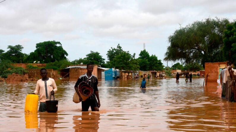 Illustration. Des personnes portent leurs affaires en marchant dans une rue inondée par les eaux du fleuve Niger qui a débordé dans le quartier de Kirkissoye à Niamey, le 27 août 2020. (Photo by BOUREIMA HAMA/AFP via Getty Images)