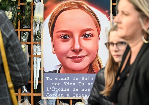 Des passants se tiennent près d'un portrait de Lola,  fillette de 12 ans qui a été violée et assassinée à Paris le 14 octobre 2022. (DENIS CHARLET/AFP via Getty Images)