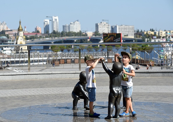 Des garçons jouent avec des sculptures décoratives représentant des enfants lors d'une chaude journée ensoleillée à Kiev, en 2018. (Photo : SERGEI SUPINSKY/AFP via Getty Images)