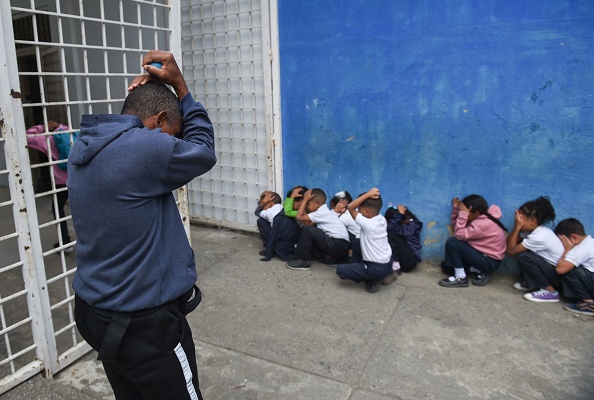 Un enseignant montre à des élèves d'une école primaire comment se couvrir la tête et le visage pendant un exercice de tir dans la cour de récréation de l'école Manuel Aguirre, à Caracas, le 23 février 2023. (MIGUEL ZAMBRANO/AFP via Getty Images)