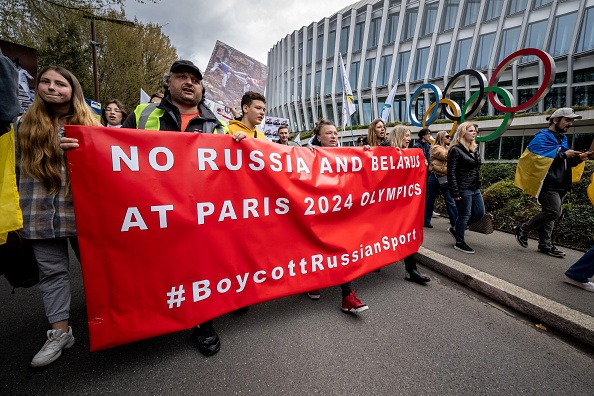 Des Ukrainiens passent devant le siège du Comité international olympique (CIO) à Lausanne, le 25 mars 2023. (FABRICE COFFRINI/AFP via Getty Images)