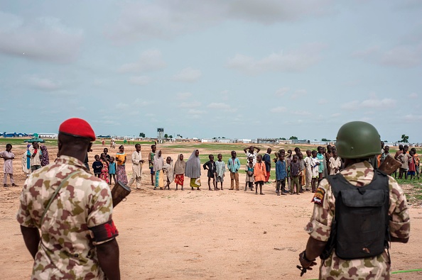 Des soldats patrouillent alors que des enfants regardent le programme de sensibilisation médicale au camp de personnes déplacées de Bakassi, au Niger. (STEFAN HEUNIS/AFP via Getty Images)
