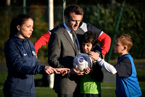 Le président Emmanuel Macron tient un ballon tout en serrant un enfant dans ses bras au stade de la Plaine à Clamart, le 4 avril 2023. (JULIEN DE ROSA/POOL/AFP via Getty Images)