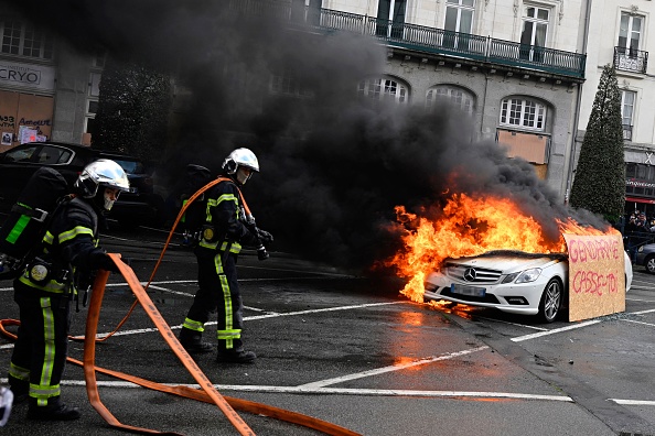 Des pompiers éteignent les flammes d'une voiture Mercedes incendiée, flanquée d'une pancarte "Gendarme, dégage", à Rennes, le 13 avril 2023. (DAMIEN MEYER/AFP via Getty Images)