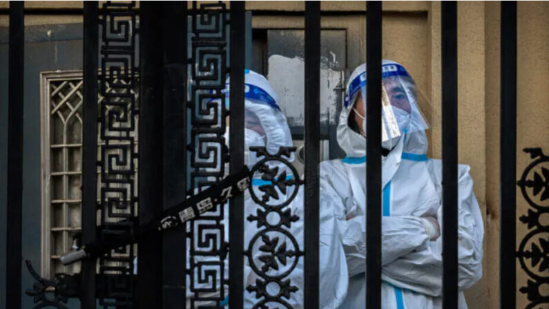 Des employés chargés de la lutte contre les épidémies montent la garde derrière la porte verrouillée d'un immeuble d'habitation situé dans le quartier central des affaires de Pékin, le 26 novembre 2022. (Kevin Frayer/Getty Images)