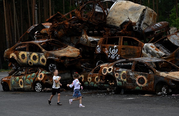 Des enfants jouent au cimetière symbolique des voitures abattues par les troupes russes, certaines peintes par des artistes locaux, à Irpin, le 9 août 2022, au milieu de l'invasion russe de l'Ukraine. (SERGEI SUPINSKY/AFP via Getty Images)