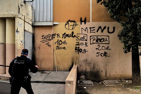 Un policier passe devant un mur avec un grafitti indiquant le prix des drogues "menu : cocaïne, herbe..." dans le quartier des Moulins à Nice. (VALERY HACHE/AFP via Getty Images)