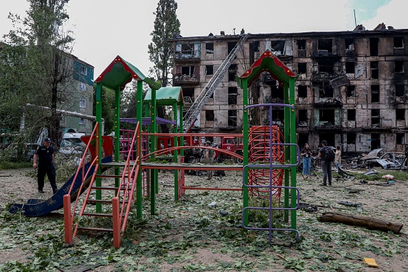 Un policier passe devant une aire de jeux pour enfants et un immeuble résidentiel détruit à la suite d'une attaque russe, à Kryvyi Rig, en Ukraine, le 13 juin 2023. (STAS YURCHENKO/AFP via Getty Images)