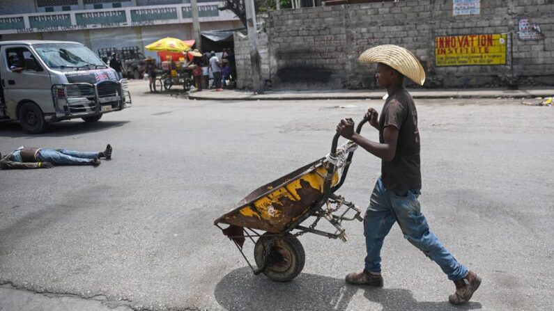 Un homme pousse une brouette, près de lui un homme mort est étendu en pleine rue, dans le centre-ville de Port-au-Prince, le 25 avril 2023.(Photo RICHARD PIERRIN/AFP via Getty Images)
