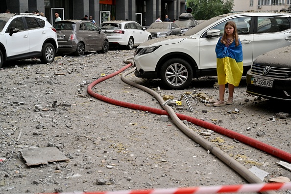 Une jeune fille marche à l'extérieur d'un immeuble de 24 étages partiellement détruit à la suite d'une frappe de missiles à Kiev, tôt le 24 juin 2023. (SERGEI SUPINSKY/AFP via Getty Images)