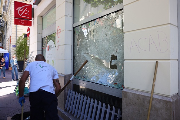 Une entreprise de nettoyage nettoie les débris à côté d'une fenêtre endommagée d'une banque Caisse d'Epargne dans le centre de Marseille, le 1er juillet 2023, après une quatrième nuit consécutive d'émeutes.   (CLEMENT MAHOUDEAU/AFP via Getty Images)