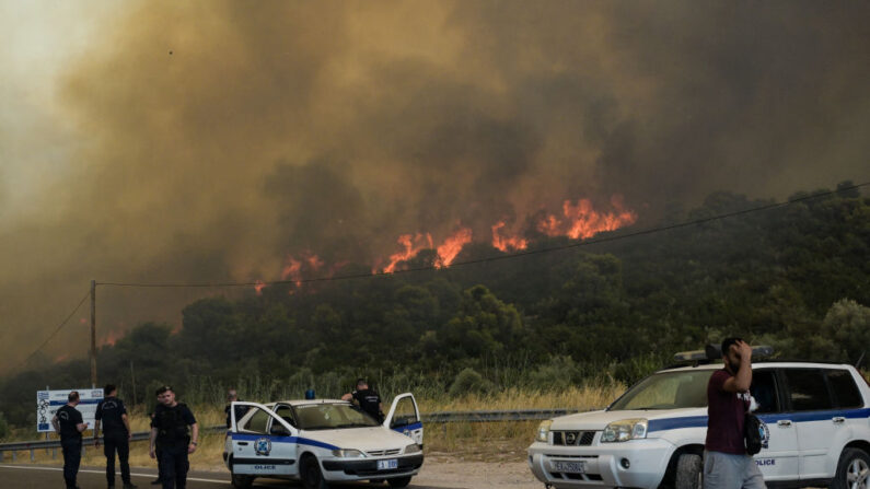 Des policiers procèdent à des évacuations alors qu'un feu de forêt brûle, dans le village d'Agios Charalabos, près d'Athènes, le 18 juillet 2023. (Photo ARIS MESSINIS/AFP via Getty Images)