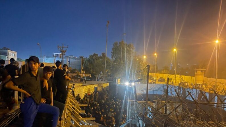 Des manifestants se tiennent sur le toit d'un bâtiment surplombant une rue remplie de policiers anti-émeutes irakiens menant à l'ambassade de Suède à Bagdad, le 20 juillet 2023. (Photo AMMAR KARIM/AFP via Getty Images)