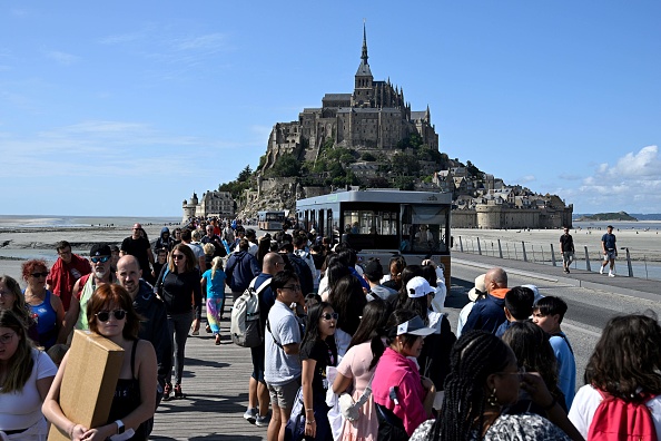 Des touristes font la queue pour prendre des bus afin de quitter le site et rejoindre les parkings au Mont-Saint-Michel, le 25 juillet 2023.  (DAMIEN MEYER/AFP via Getty Images)