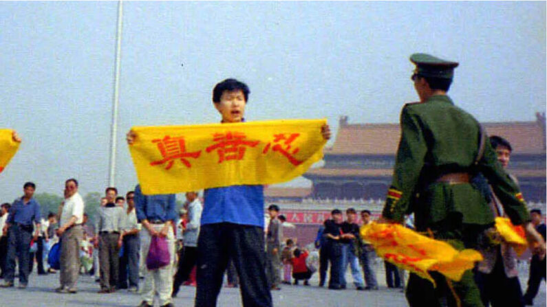 Un policier chinois s'approche d'un pratiquant du Falun Gong sur la place Tiananmen à Pékin, alors qu'il tient une bannière sur laquelle figurent les caractères chinois "vérité, compassion et tolérance", les principes fondamentaux du Falun Gong. (Avec l'aimable autorisation de Minghui)