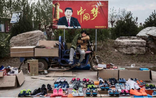 Un vendeur de rue vend des baskets et des chaussures devant un panneau avec l’image du dirigeant chinois Xi Jinping et les mots "Rêve chinois", à Shijiazhuang, dans la province chinoise du Hebei, le 9 avril 2017. (Kevin Frayer/Getty Images)