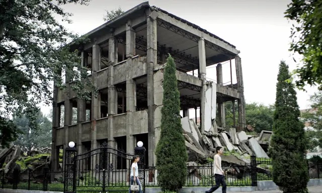 Des étudiants passent devant les ruines de la bibliothèque universitaire, aujourd'hui transformée en mémorial du tremblement de terre, sur le campus universitaire de Tangshan, dans la province chinoise du Hebei (nord-est), le 19 juillet 2006. Plus de 240.000 personnes sont mortes lors d'un puissant tremblement de terre qui a frappé la ville de Tangshan le 28 juillet 1976. (Peter Parks/AFP via Getty Images)