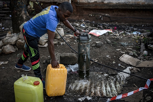 Un homme remplit des bidons d'eau potable près du bidonville du quartier "Talus 2" à Koungou. (Photo PHILIPPE LOPEZ/AFP via Getty Images)