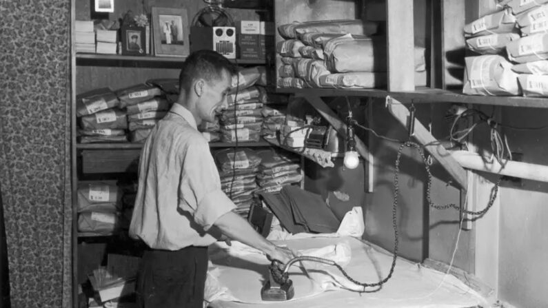 Un employé repasse une chemise entouré d'étagères sur lesquelles sont posés des vêtements propres enveloppés dans du papier brun, vers 1945. (Lawrence Thornton/Getty Images)
