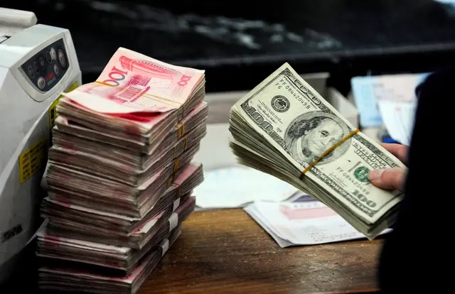 Un employé de banque chinois se prépare à compter une pile de dollars américains et des piles de billets de 100 yuans chinois dans une banque à Hefei, dans la province d'Anhui, en Chine, le 9 mars 2010. (STR/AFP via Getty Images)