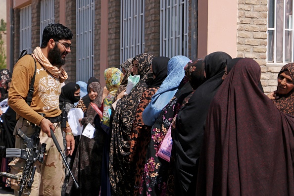 Un agent de sécurité taliban au côté des femmes devant le bureau des passeports à Herat, le 26 août 2023. (Photo MOHSEN KARIMI/AFP via Getty Images)