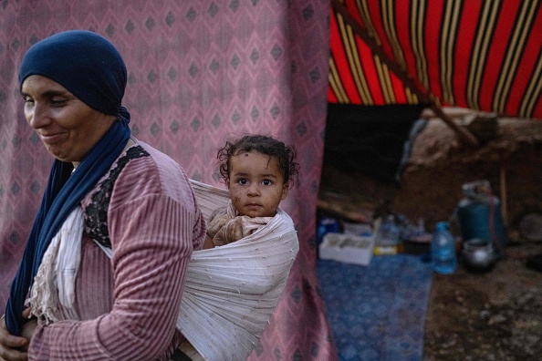 Une femme portant son bébé se tient devant une tente de fortune dans son village de la région montagneuse de Tizi N'Test, au Maroc. (Photo BULENT KILIC/AFP via Getty Images)