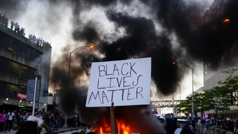 Un homme tient une pancarte Black Lives Matter alors qu'une voiture de police brûle devant lui lors d'une manifestation pour la mort de George Floyd, devant le centre CNN à Atlanta, le 29 mai 2020. (Elijah Nouvelage/Getty Images)