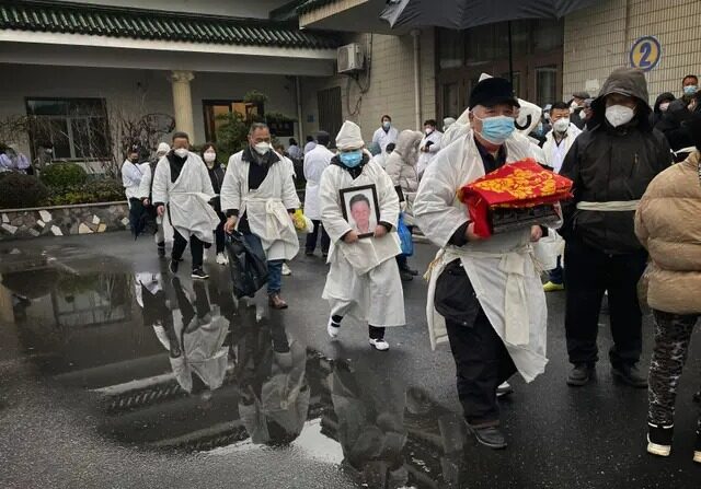 Une personne en deuil porte les restes incinérés d'un être cher alors qu'elle et d'autres participants portent des vêtements funéraires blancs traditionnels lors d'un enterrement à Shanghai, en Chine, le 14 janvier 2023. (Kevin Frayer/Getty Images)