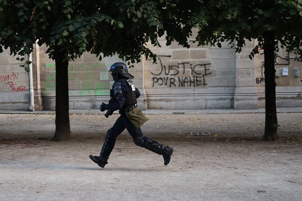 Un CRS passe devant un graffiti "Justice pour Nahel" dans le jardin des Tuileries à Paris le 30 juin 2023.  (CHARLY TRIBALLEAU/AFP via Getty Images)