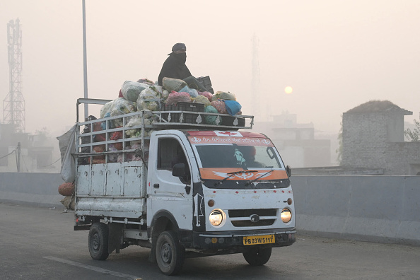 Un vendeur indien assis sur un camion de légumes se couvre le visage avec un tissu dans un smog dense le long d'une rue à Amritsar le 24 novembre 2023. (Photo NARINDER NANU/AFP via Getty Images)