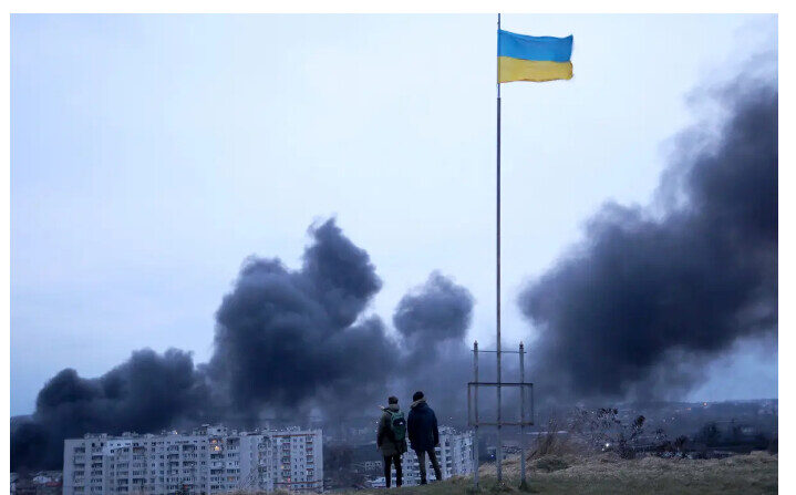 Des gens se tiennent près d'un drapeau national ukrainien en observant la fumée noire qui se dégage après une frappe aérienne russe dans la ville de Lviv, dans l'ouest de l'Ukraine, le 26 mars 2022. (Oleksii Filippov/AFP via Getty Images)