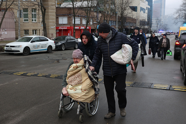 Des habitants aident un homme handicapé évacué après une attaque de missiles dans le centre de Kiev, le 2 janvier 2024. (Photo ANATOLII STEPANOV/AFP via Getty Images)