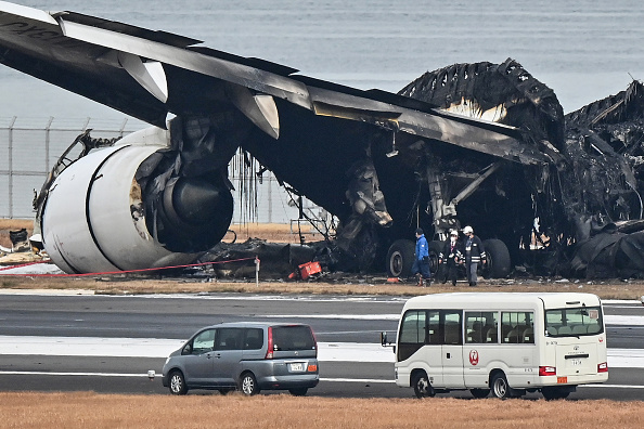 Des officiels regardent l'épave brûlée d'un avion de passagers de Japan Airlines (JAL) sur le tarmac de l'aéroport international de Tokyo à Haneda à Tokyo le 3 janvier 2024. (Photo RICHARD A. BROOKS/AFP via Getty Images)