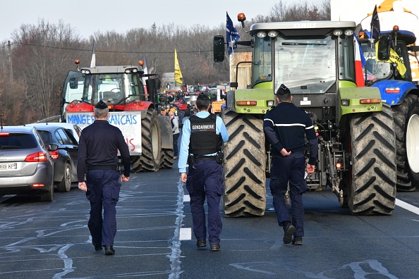 Des gendarmes passent devant des tracteurs alors que des agriculteurs bloquent l'autoroute A20 près d'Argenton-sur-Creuse, le 30 janvier 2024. (Photo PASCAL LACHENAUD/AFP via Getty Images)