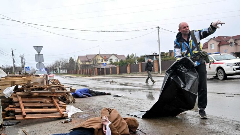 Le corps d'un civil, les mains attachées dans le dos par un tissu blanc, gît dans la rue alors qu'un employé communal prépare un sac mortuaire en plastique pour le transporter dans une voiture qui attend, dans la ville de Bucha, non loin de la capitale ukrainienne de Kiev, le 3 avril 2022. (SERGEI SUPINSKY/AFP via Getty Images)