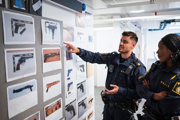 Deux officiers de police pointent un tableau montrant des images d'armes saisies au poste de police de Rinkeby, Suède. Ces dernières années, les fusillades entre gangs se sont multipliées et étendues à toute la Suède. (Photo by JONATHAN NACKSTRAND/AFP via Getty Images)