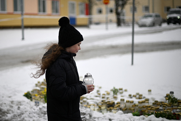 Une jeune fille dépose une bougie sur un mémorial improvisé devant l'école Viertola à Vantaa, au nord de la capitale finlandaise Helsinki, le 3 avril 2024. (Photo OLIVIER MORIN/AFP via Getty Images)