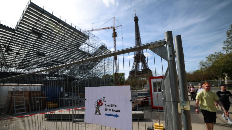 À Paris le 12 avril 2024, des piétons passent devant des travaux de construction fermés avec la Tour Eiffel en arrière-plan sur le Champ-de-Mars qui accueillera la compétition de beach-volley lors des prochains Jeux Olympiques de Paris 2024. (Photo EMMANUEL DUNAND/AFP via Getty Images)
