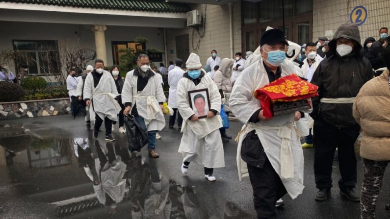Une personne en deuil porte les restes incinérés d'un être cher alors qu'elle et d'autres portent des vêtements funéraires blancs traditionnels, lors d'un enterrement à Shanghai, en Chine, le 14 janvier 2023. (Kevin Frayer/Getty Images)