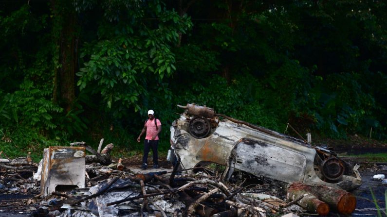 Un homme marche devant des épaves de voitures incendiées pendant la nuit à Fort-de-France, sur l'île française de la Martinique, dans les Caraïbes, le 13 octobre 2024. (PHILIPPE LOPEZ/AFP via Getty Images)