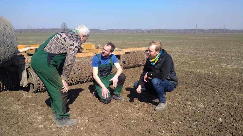 Les agriculteurs allemands Tim Nandelstädt (au c.) et Torben Reelfs (à dr.) inspectent le champ de leur ferme à Derzhiv, dans le raion de Stryi, dans l'oblast de Lviv, dans l'ouest de l'Ukraine, le 23 mars 2022. (Tim Nandelstaedt/AFP via Getty Images)